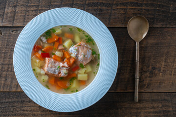 Fresh salmon fish soup with carrots, potatoes and red peppers in a white plate, close up. Tasty dinner consists of a fish soup with salmon. Top view