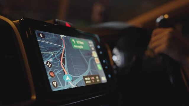 Close up hand driving car and turning on GPS, display screen traffic jam map GPS navigation system in car at night time.