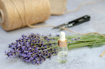 Fototapeta na wymiar Bottle with cosmetic oil in front of a bouquet of lavender on a gray background. Lavender essential oil for body and hair care. Making a bouquet of fresh lavender.