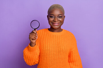Photo of cute young lady holding enlarge loupe looking wear trendy orange autumn knitted pullover specs isolated on purple color background