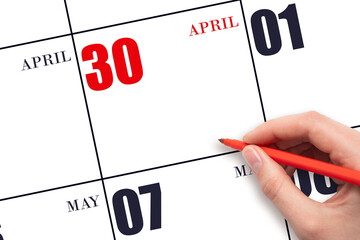 A hand holding a red pen and pointing on the calendar date April 30. Red calendar date, copy space,...