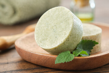 Nettle solid shampoo pieces or homemade natural organic soap bars on wooden soap dish, fresh green nettle leaves. A bath towel, essential oil bottle and comb on background. Selective focus. - 531994053