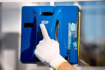 Hand of a window washer in a white glove presses the start button to start the robot. Close-up of...