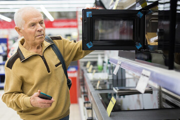 senor man pensioner buying microwave oven in showroom of electrical appliance store