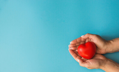 Women's hands hold a small red heart on a blue background, on the left is a copyspace.The concept of a thrifty attitude to the heart, woman's health. Give  care. mother's day, loving female heart