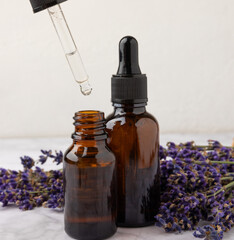 Essential oil of lavender in a glass bottle with a pipette on a white texture background.Bottle...