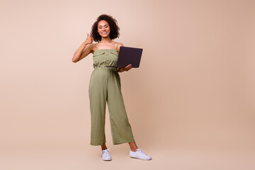 Full size photo of cool brunette woman hold laptop thumb up wear khaki overall isolated on beige color background