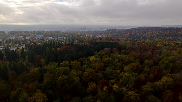 Aerial time lapse shot of a colorful forest near Ulm city with Ulm minster in the background on a cloudy morning in autumn.