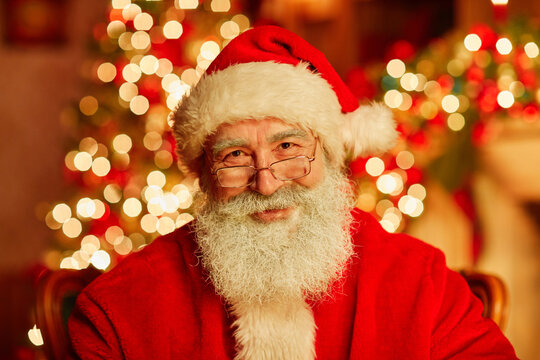 Close up portrait of traditional Santa Claus smiling at camera with twinkling Christmas lights in background