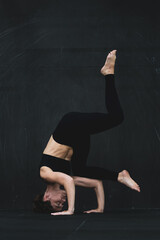 Young woman meditates, doing yoga poses and asana. Fitness girl enjoying yoga indoors. A yoga gymnast girl on a dark background. Black on Black