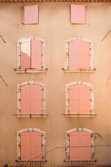 Window wooden pink shutters on pastel orange color painted wall building.