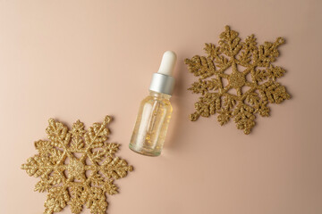 A natural transparent hyaluronic face serum with golden parts and two golden snowflakes lying on a beige background