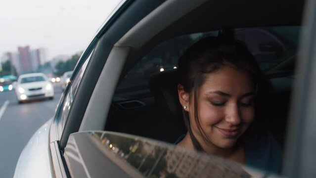 A young beautiful woman rides in a taxi with an open window, smiles, takes a photo of the street on her phone. Road, trip, car. Slow motion 4k footage
