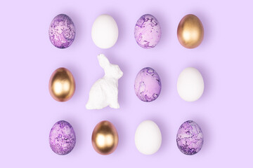 Happy Easter concept. White, gold, violet Easter eggs and bunny on violet background. Minimalism flat lay top view copy space banner.