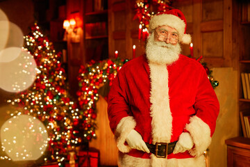 Waist up portrait of traditional Santa Claus looking at camera while standing in room with...