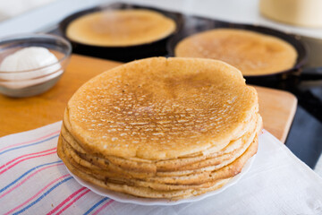 hot golden pancakes made from grain flour in kitchen while cooking on pans and on plate