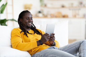 Handsome Young Black Man With Digital Tablet Relaxing On Couch At Home