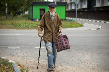 Grandfather crosses road. Grandfather with stick. Man with gray beard on street. Retired in Russia....