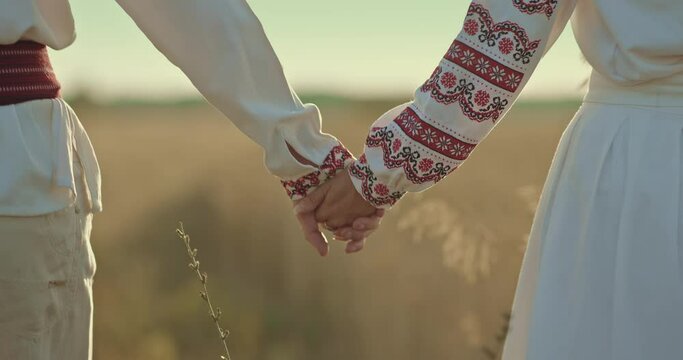 Close-up, a man and a woman Slavs holding hands and walking across the field, a happy family. People in folklore costumes holding each other's hands, walking. 4k, ProRes