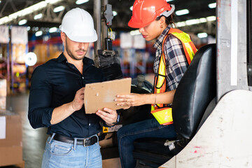 Male factory foreman holding document discuss and explain work project to female worker on forklift in the industry warehouse. Logistic shipping delivery career. © winnievinzence