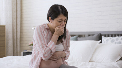 asian pregnant female with her hand on the stomach and mouth is feeling nausea and almost throwing...