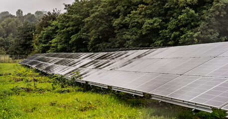 Wielkopowierzchniowe panele solarne w deszczu wśród drzew . Mała elektrownia słoneczna .  