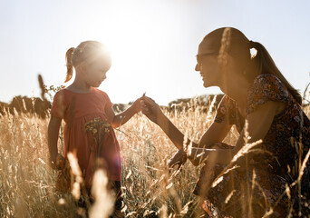 Portrait of cute happy little girl and her mother playing in a grass meadow at sunset. Motherhood...