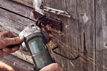 A man cuts a lock on an old door of a house with an angle grinder.