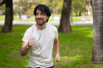 Portrait of handsome attractive mature bearded athletic latin man guy 40s in casual white t-shirt running at a park, looking aside