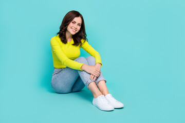 Full size portrait of satisfied glad girl toothy beaming smile sit floor isolated on teal color...