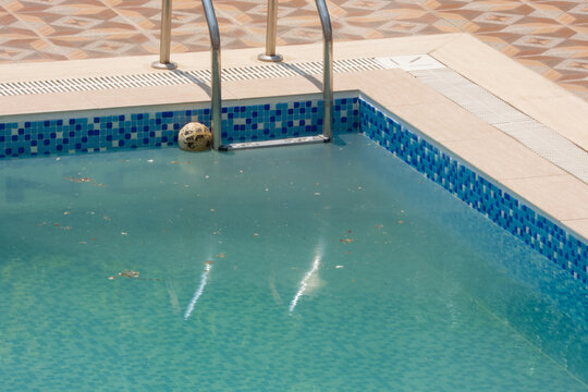 An old ball floats in a pool of dirty water on a sunny day
