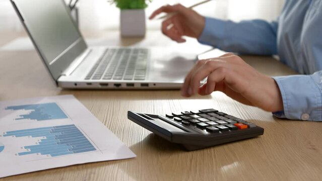 The hand of a financial manager is counting on a calculator using a laptop.