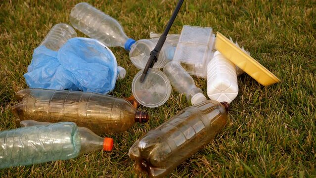 Close-up of volunteers collecting plastic garbage with tongs on the grass in the park. The concept of volunteering and environmental protection.