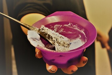 Hand von Frisörin mit schwarzer Bluse hält pinke Plastikschüssel mit weißer Haarfarbe und schwarzem Pinsel in Frisörsalon