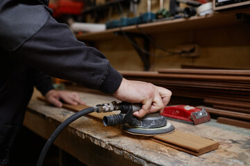 Close up of unrecognizable male worker sanding wooden boards in workshop and using electric tools, copy space