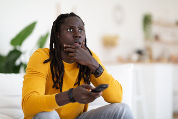 Portrait Of Shocked Black Man With Remote Controller In Hand At Home