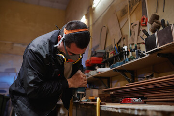 Portrait of young factory worker wearing respirator while sanding wood in workshop, copy space