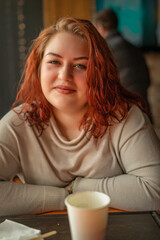 Close-up portrait of a young beautiful red-haired plump girl in a cafe.