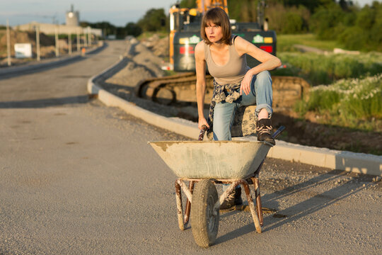 Junge Frau steht mit einer Schubkarre vor einer Baumaschine.