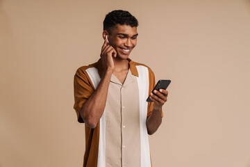 Young african handsome smiling man in wireless headphones using phone