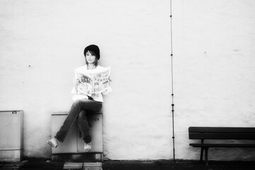 Eine hübsche Frau sitzt im Herbst auf einem Stromverteiler, und liest Zeitung-