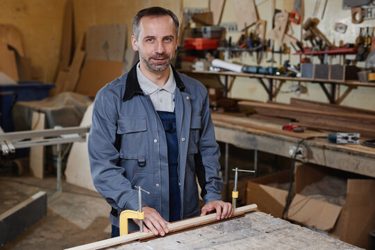 Waist Up Portrait Of Mature Male Worker Looking At Camera While Working With Wood In In Factory Workshop, Copy Space