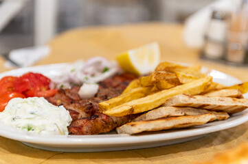 Fried meat souvlaki, fresh vegetables, pita bread, tzatziki sauce and french fries, traditional greek food served in cafe