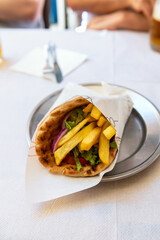 Greek vegetarian gyros with french fries, halloumi cheese and fresh vegetables wrapped in pita and served in greek cafe