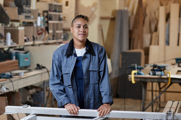Waist up portrait of female worker standing in factory workshop and looking at camera, copy space