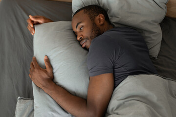 Fototapeta premium Tired African Male Lying Having Sleeplessness In Bedroom, High Angle