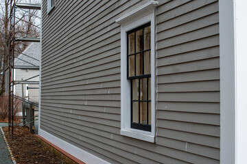 Old tan colored house with white trim and black wood window frame spacers. The glass in the window...