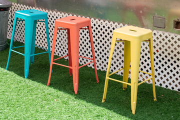 Three colorful iron metal stackable bar stools, blue, peach, and yellow color. The chairs are on...