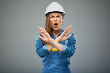 Shouting woman in safety helmet and overall doing stop gesture with hands. Isolated female portrait.