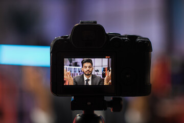 View from camera screen of relaxed motivated indian businessman in formal wear meditating with closed eyes and mudra hands in front of camera during recording video for business vlog in evening office - obrazy, fototapety, plakaty
